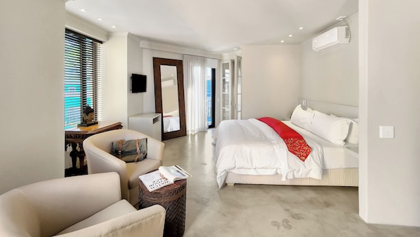 A modern hotel room with a large bed, a seating area with a chair, a small table, and a large mirror. - Rouge on Rose Boutique Hotel (Cape Town)