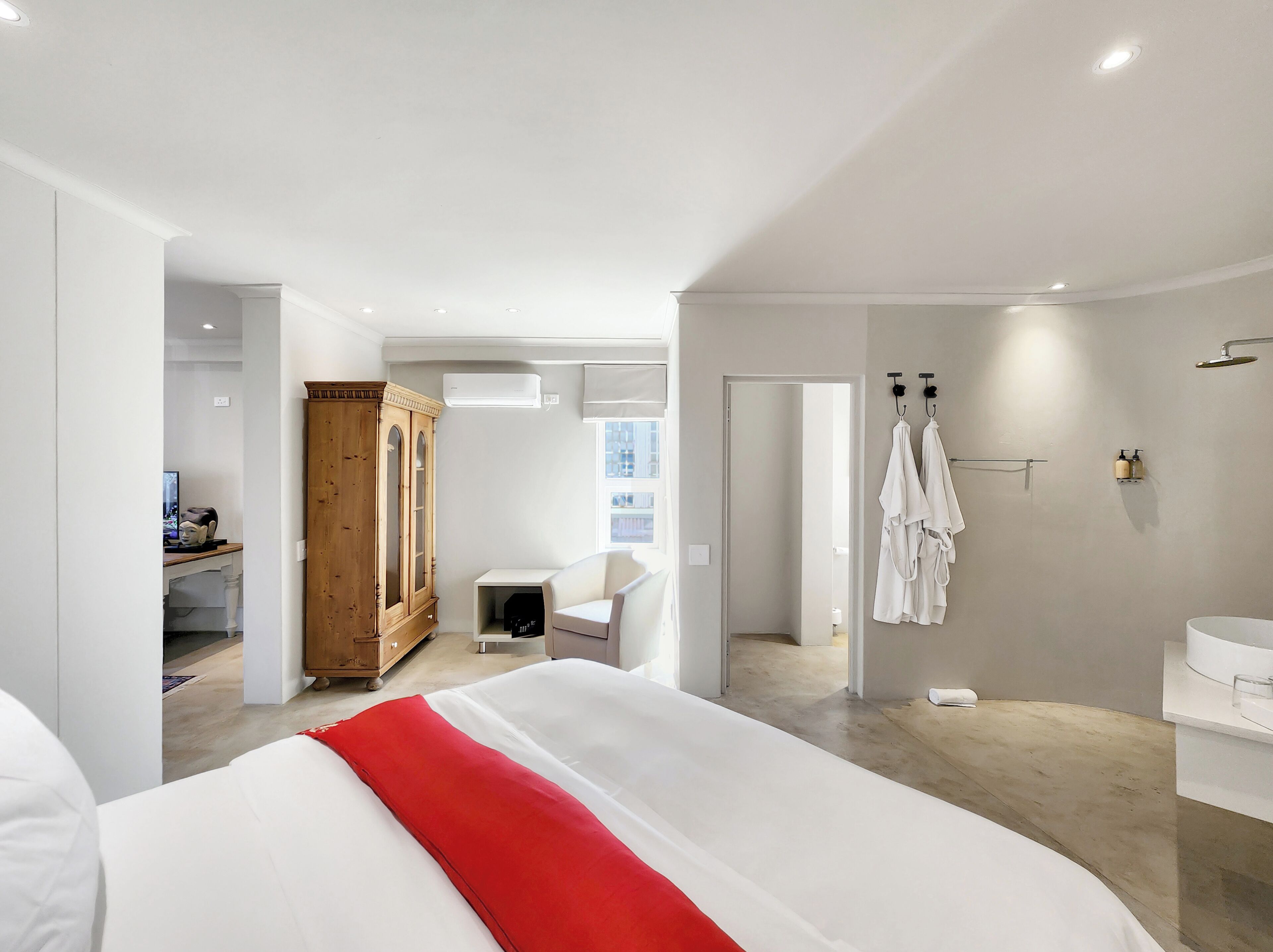 A modern hotel room with a large bed, a wooden wardrobe, a desk with a computer, a bathroom with a shower, and a view of the outside.