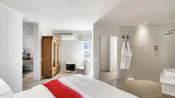 A modern hotel room with a large bed, a wooden wardrobe, a desk with a computer, a bathroom with a shower, and a view of the outside.