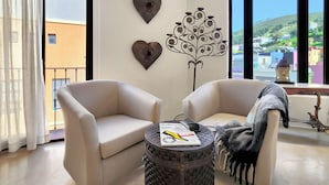 A modern living room with two beige armchairs, a round coffee table with a magazine, and decorative wall art. - Rouge on Rose Boutique Hotel (Cape Town)