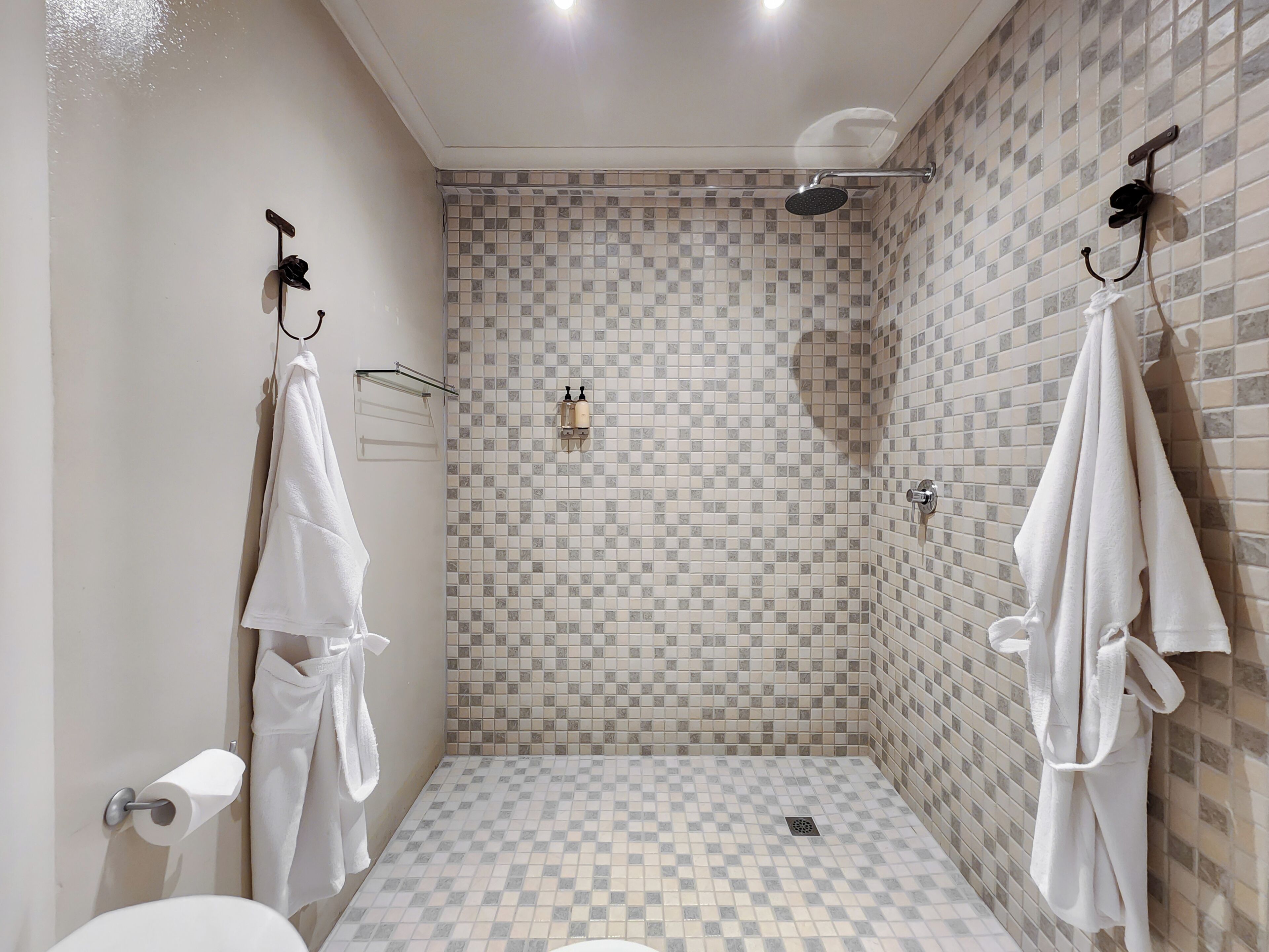 A bathroom with a checkered floor, a shower, and two towels hanging on hooks.