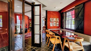 A dining area with a glass door leading to a corridor, a black tiled floor, and a red wall with framed pictures. - Rouge on Rose Boutique Hotel (Cape Town)