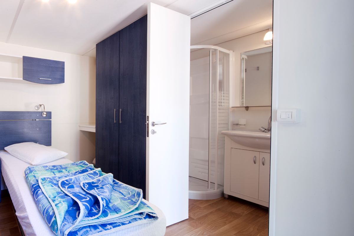 Une chambre à coucher comprenant un lit, une armoire, une salle de bain avec un lavabo et un miroir, et une porte donnant sur une autre pièce.