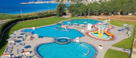 Una gran piscina al aire libre con varias secciones, incluyendo una piscina circular central y una zona de toboganes.
