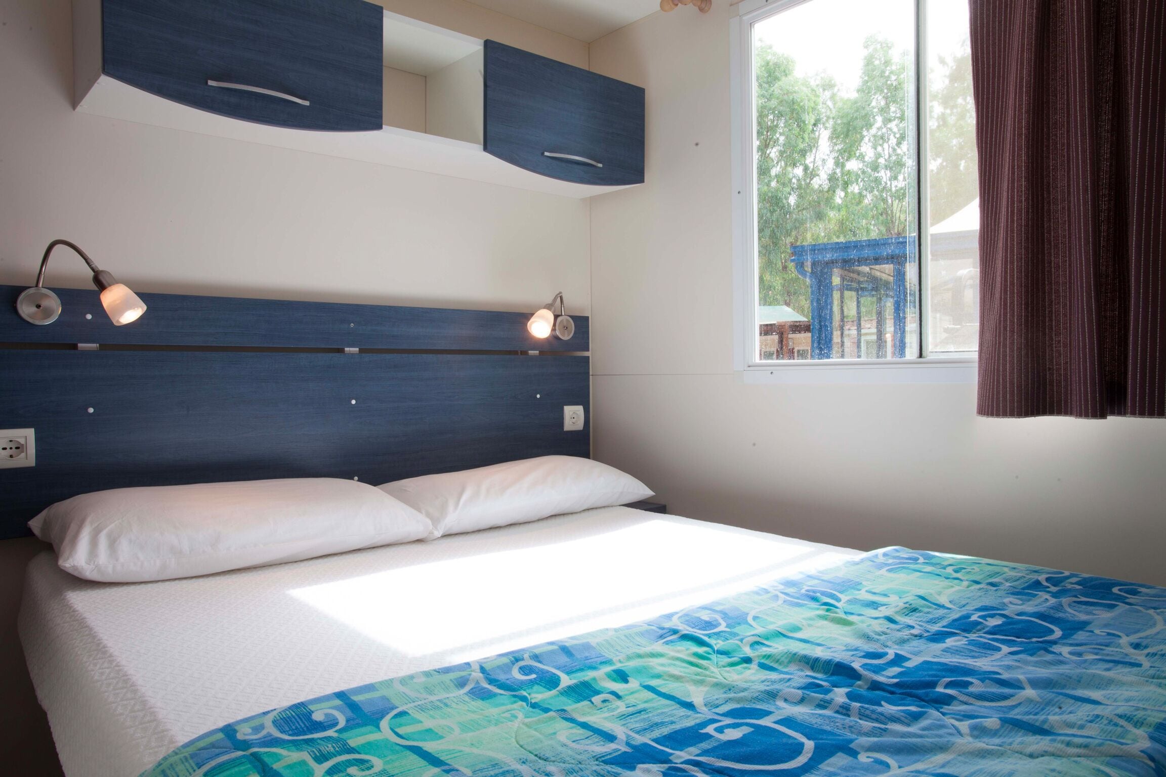 A bedroom with a bed, two bedside lamps, a window with curtains, and built-in cabinets.