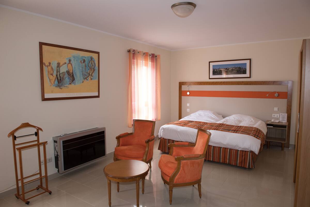 Habitación de hotel con cama, dos sillones, una mesita, un radiador y dos cuadros en la pared.