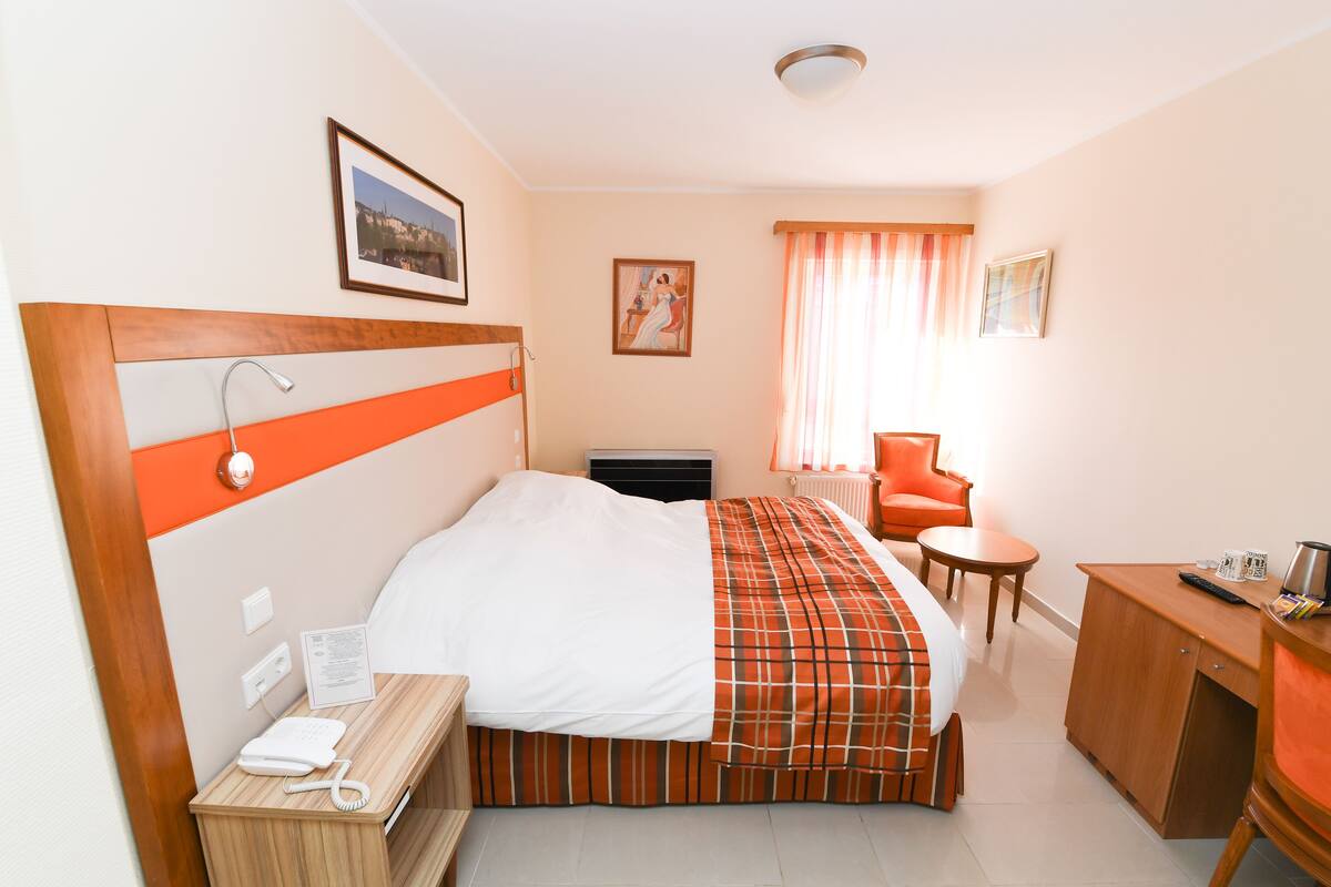 Una habitación de hotel con cama, escritorio, silla, teléfono y radiador.