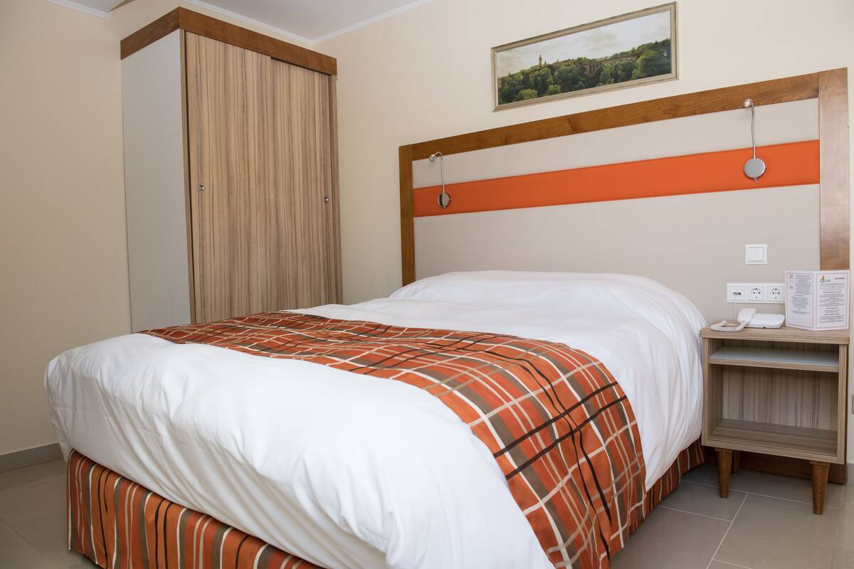Una habitación de hotel con una cama, una mesita de noche, un armario de madera y un cuadro en la pared.