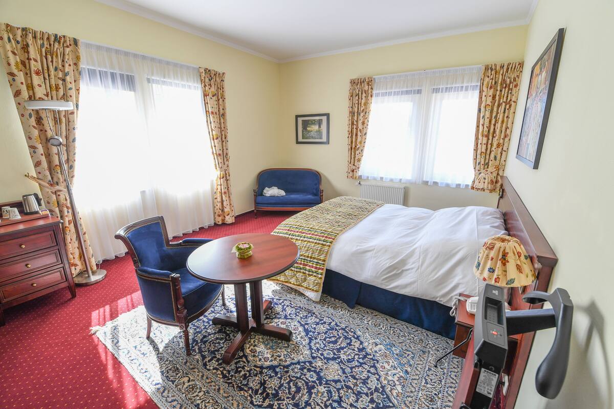 Habitación de hotel con cama, escritorio, silla, lámpara y ventana con cortinas.