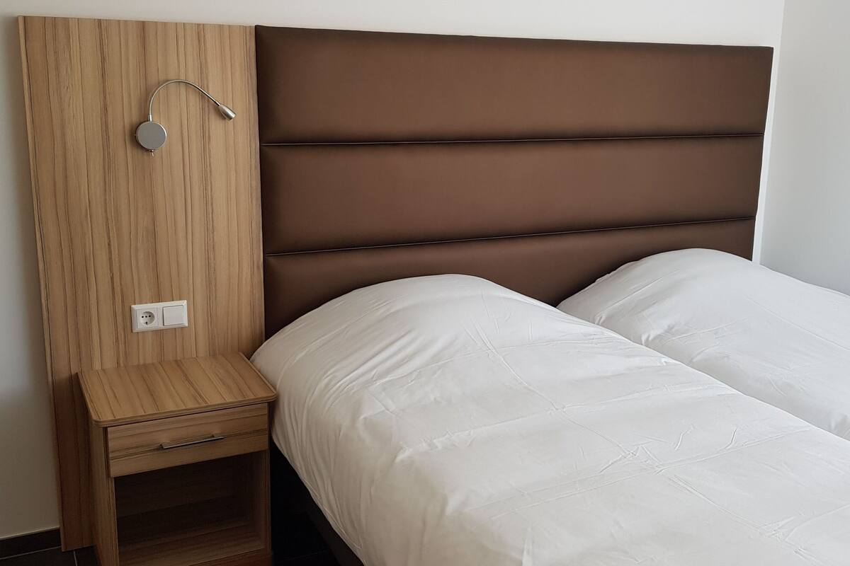 Un dormitorio con una mesita de noche de madera, un cabecero marrón y una cama blanca.