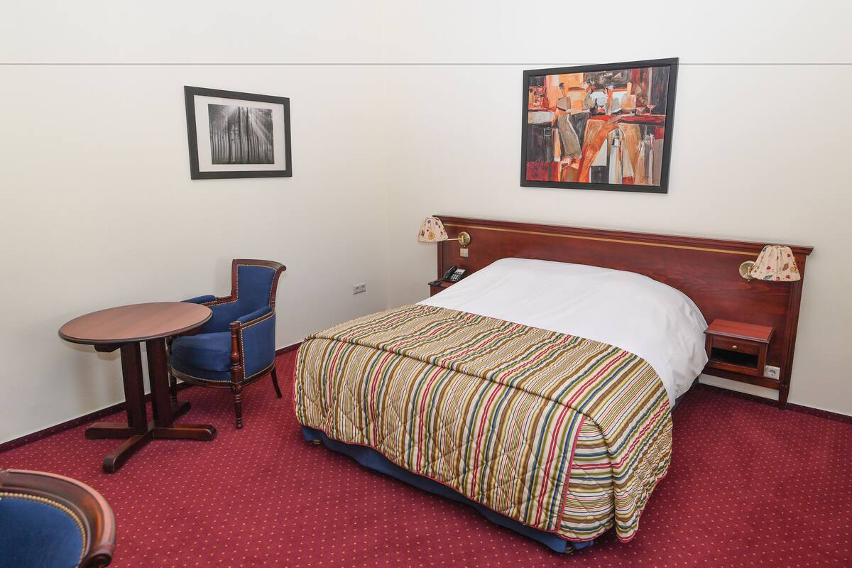 Habitación de hotel con cama, una silla, una mesita y dos lámparas de pared.