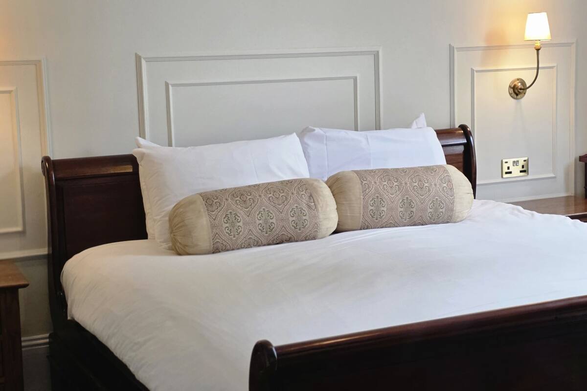 A neatly made bed with white and patterned pillows, a wooden headboard, and a nightstand with a lamp.