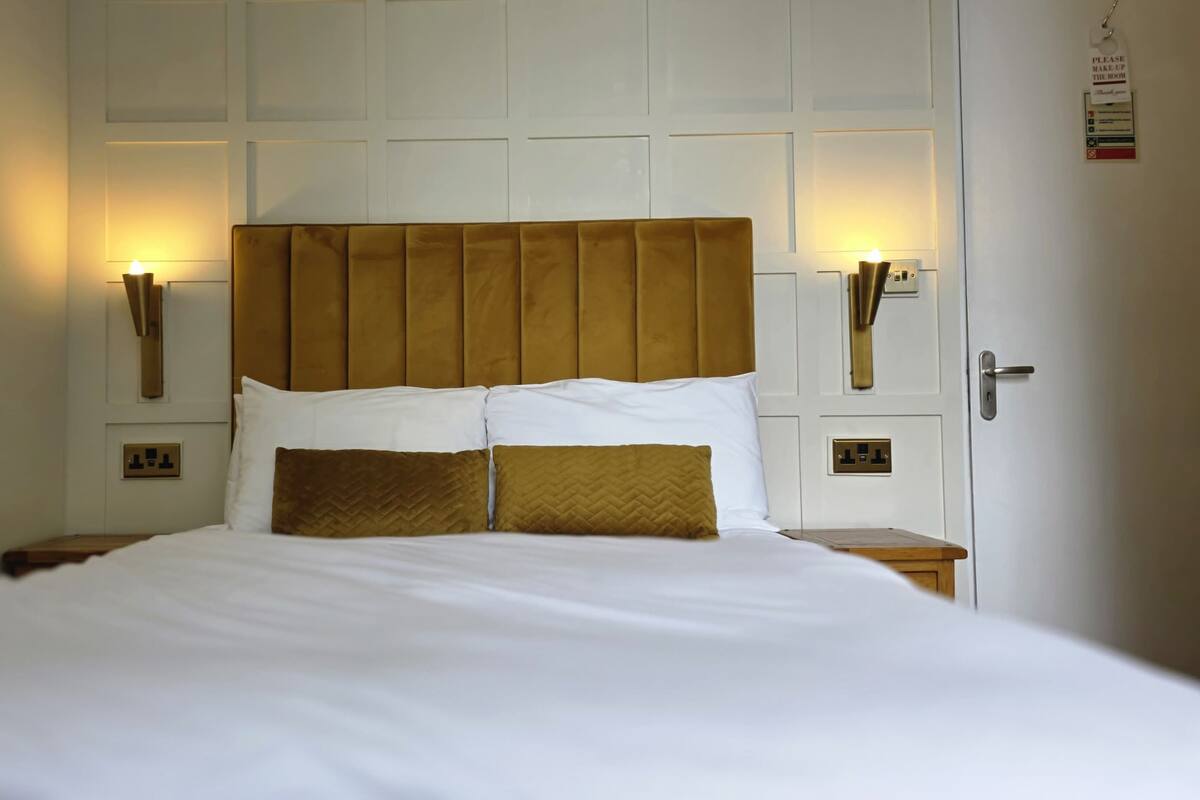 A neatly made bed with a headboard, two bedside lamps, and a door with a sign.