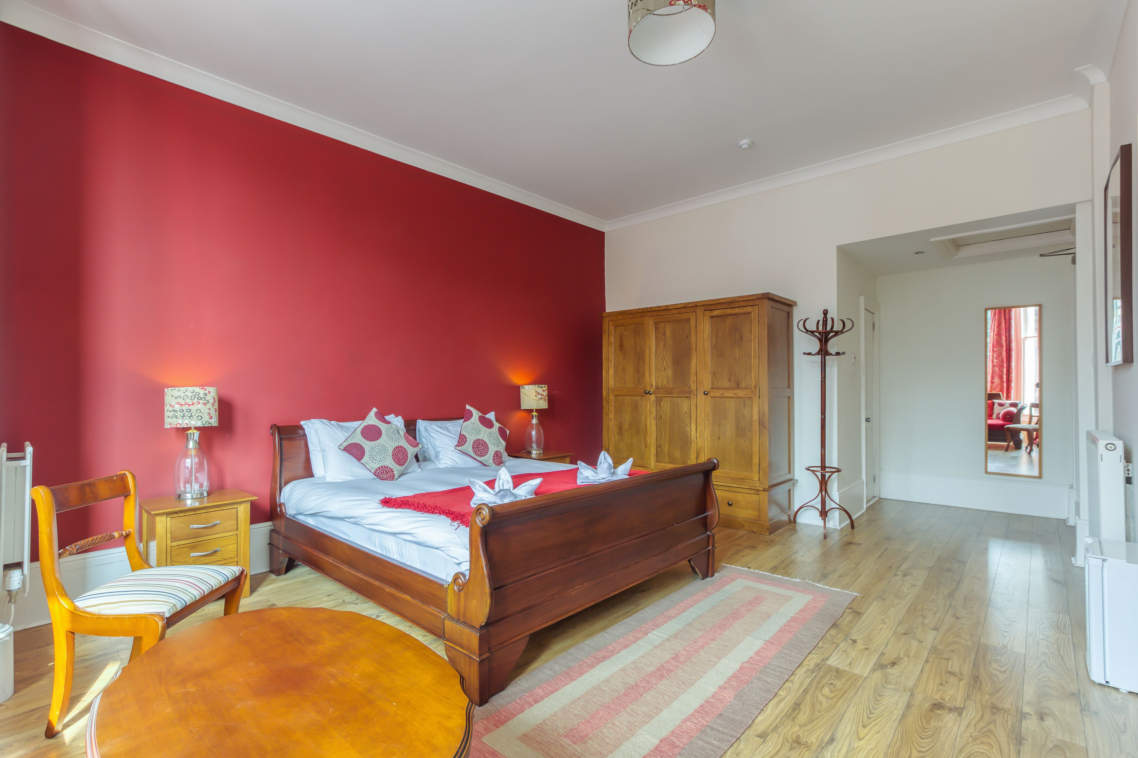 A bedroom with a wooden bed, a nightstand, a chair, a wardrobe, and a mirror.