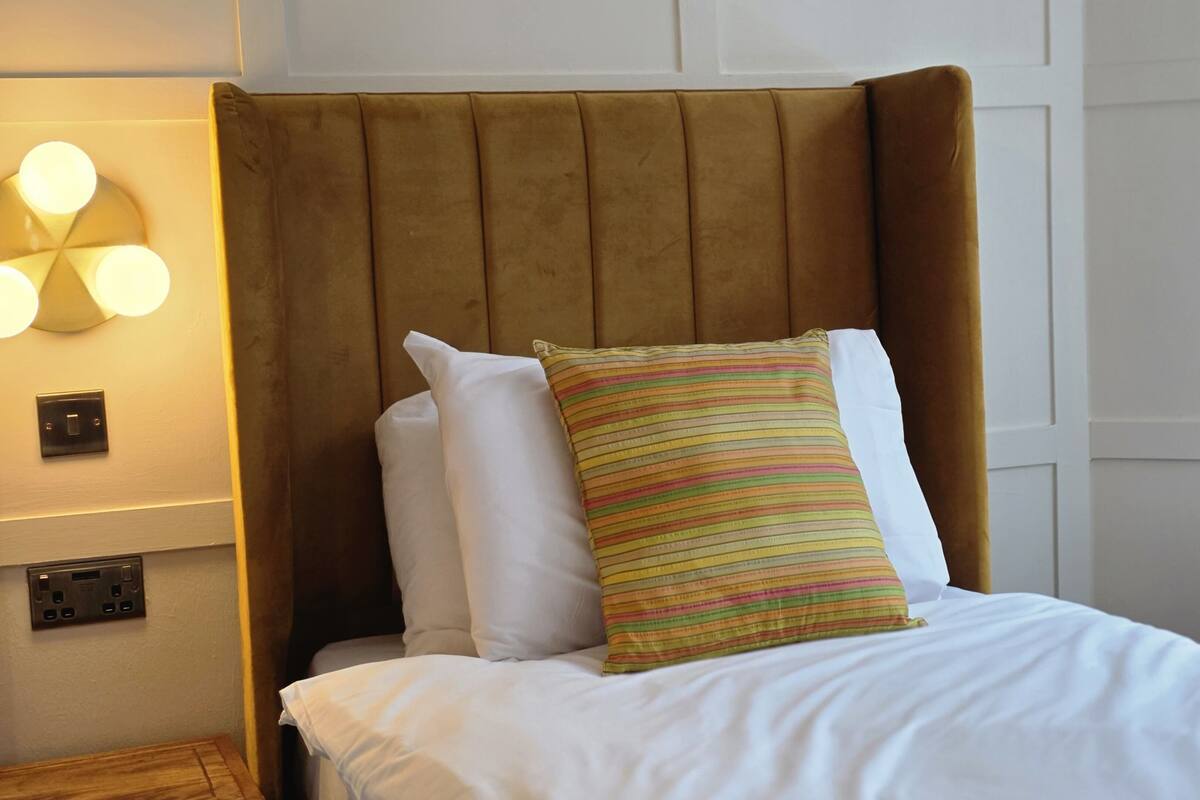 A bed with white bedding, a striped pillow, and a brown headboard.