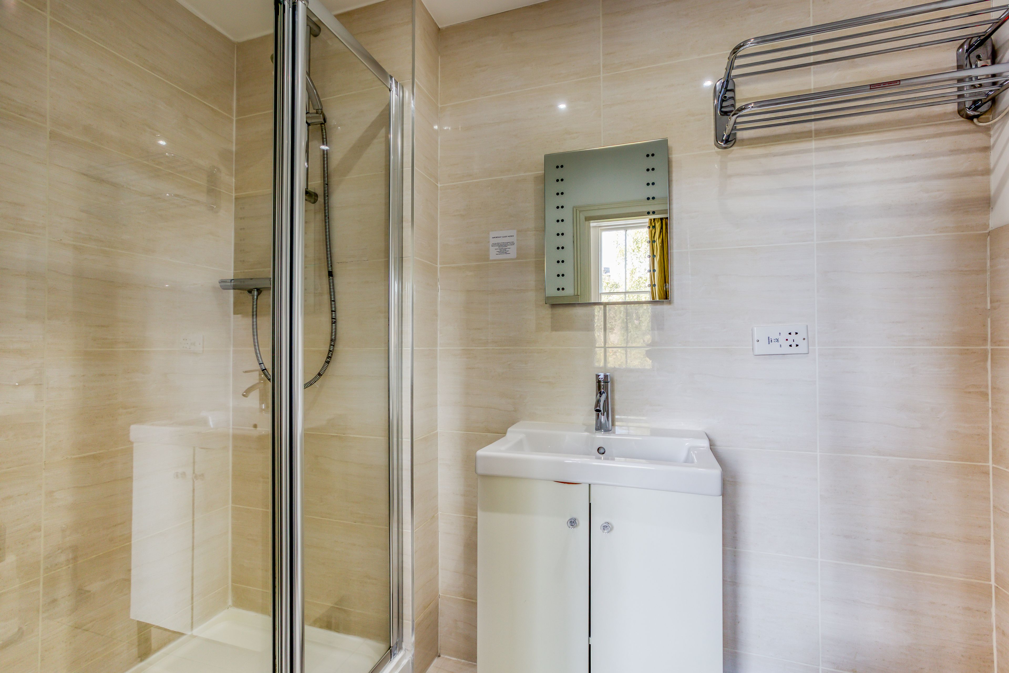 Un baño con ducha de vidrio, un lavamanos blanco con espejo y un perchero en la pared.