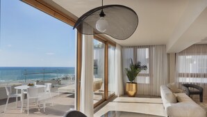 A modern living room with a large window overlooking the ocean, a round table with chairs, a sofa, and a potted plant. - Jewel Beachfront Boutique Hotel (Tel Aviv)