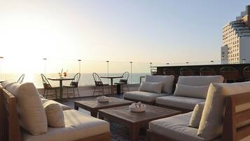 A rooftop terrace with outdoor seating, including sofas and chairs, overlooking a body of water.