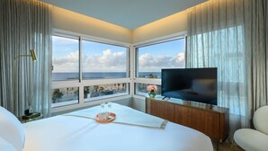 A hotel room with a large bed, a TV, a wooden cabinet, and a view of the sea. - Jewel Beachfront Boutique Hotel (Tel Aviv)