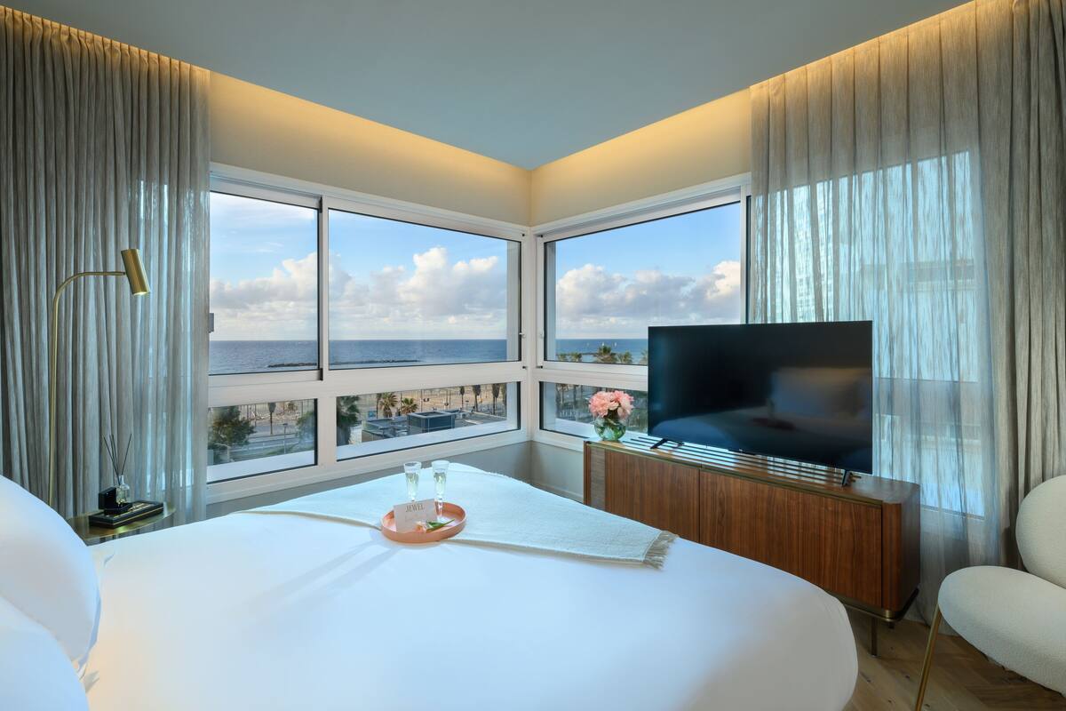 Habitación de hotel con una cama grande, televisión, mueble de madera y vista al mar.