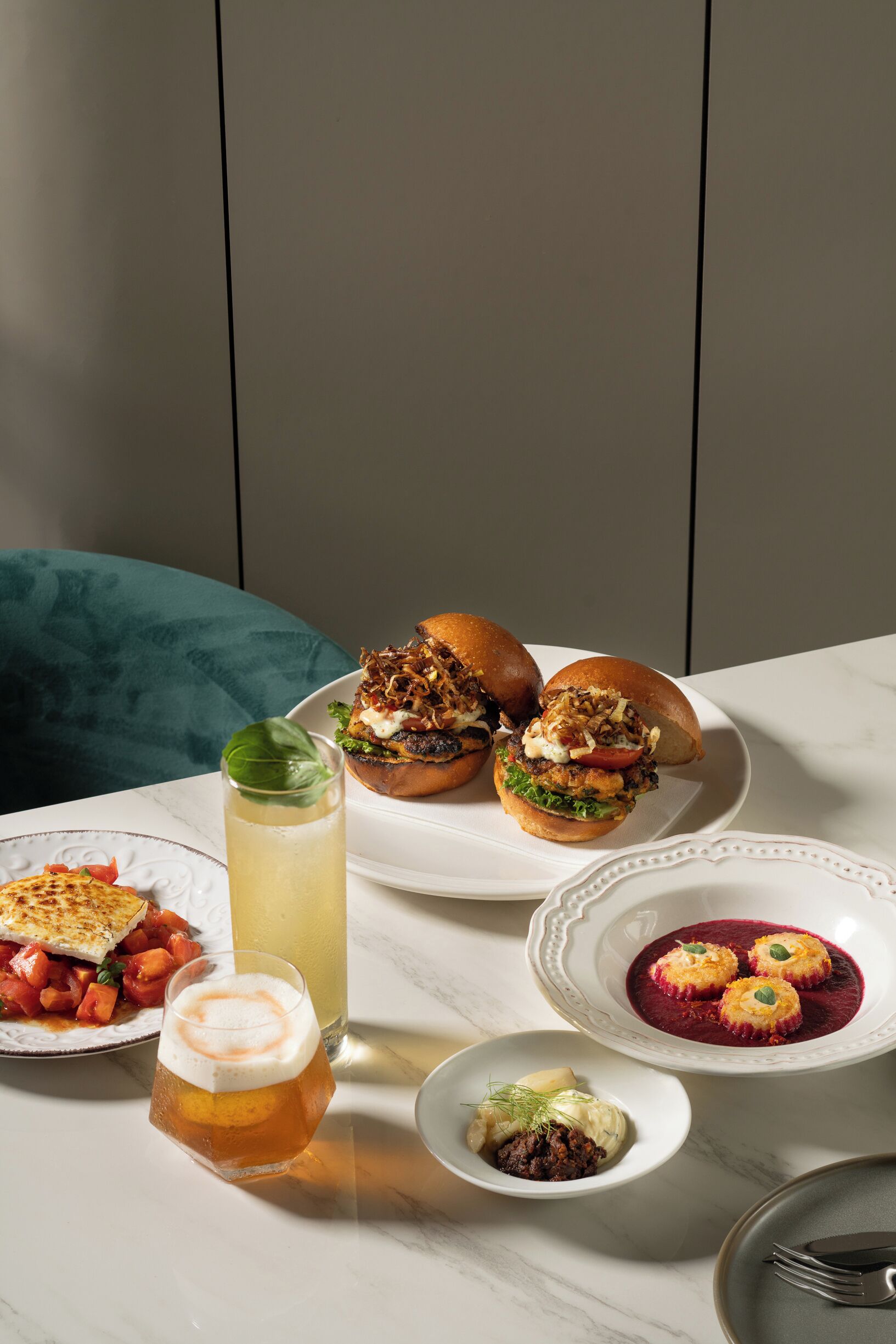 A table with food and drinks, including burgers, a glass of beer, and a bowl of soup.