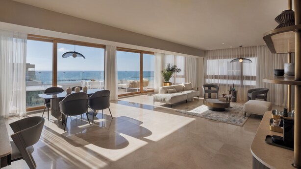 A spacious living area with a large window overlooking the sea, a modern sofa, a dining table, and a coffee table. - Jewel Beachfront Boutique Hotel (Tel Aviv)