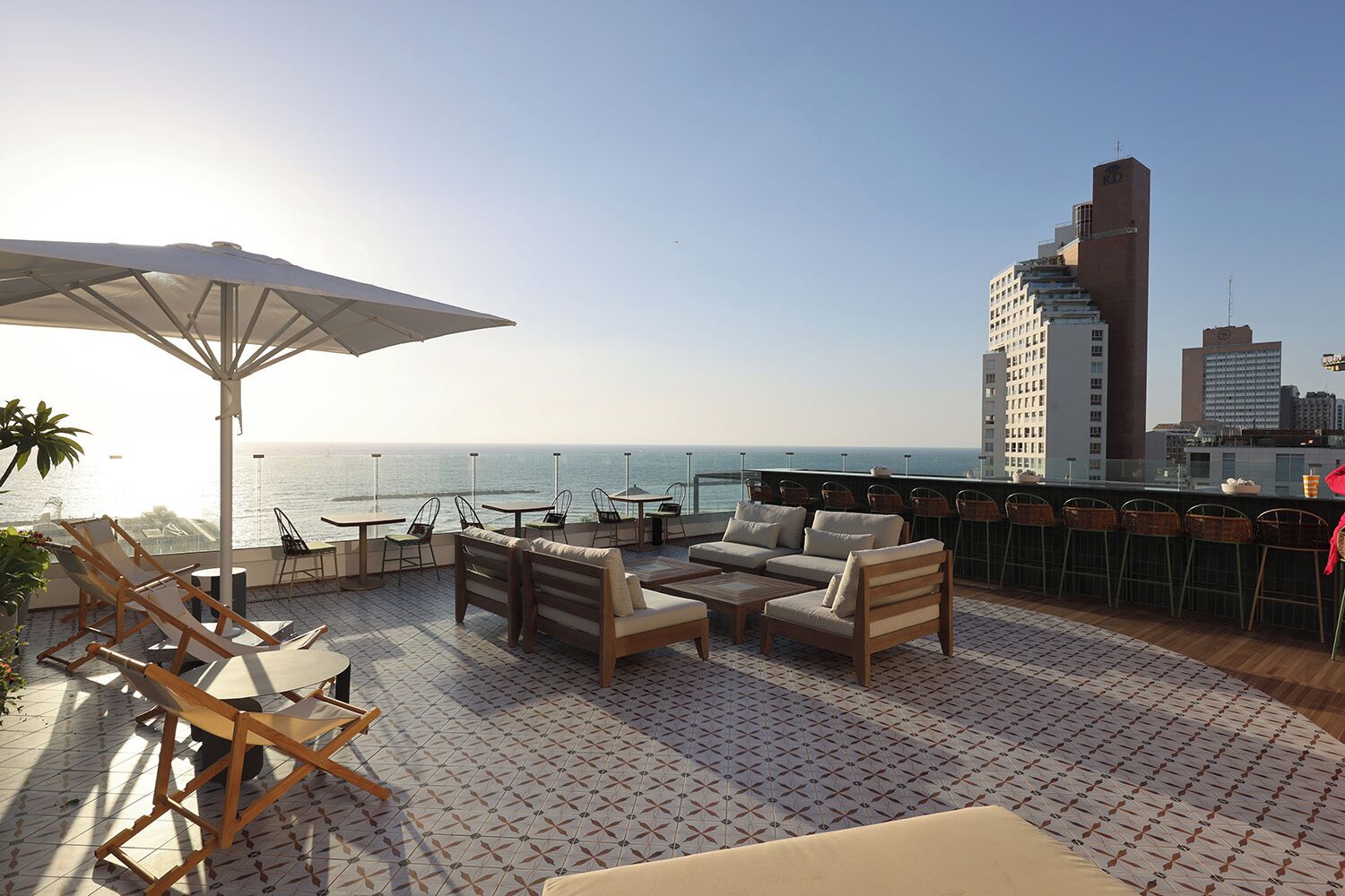 Una terraza en la azotea con mobiliario exterior, un paraguas grande y vistas al océano y al horizonte de la ciudad.