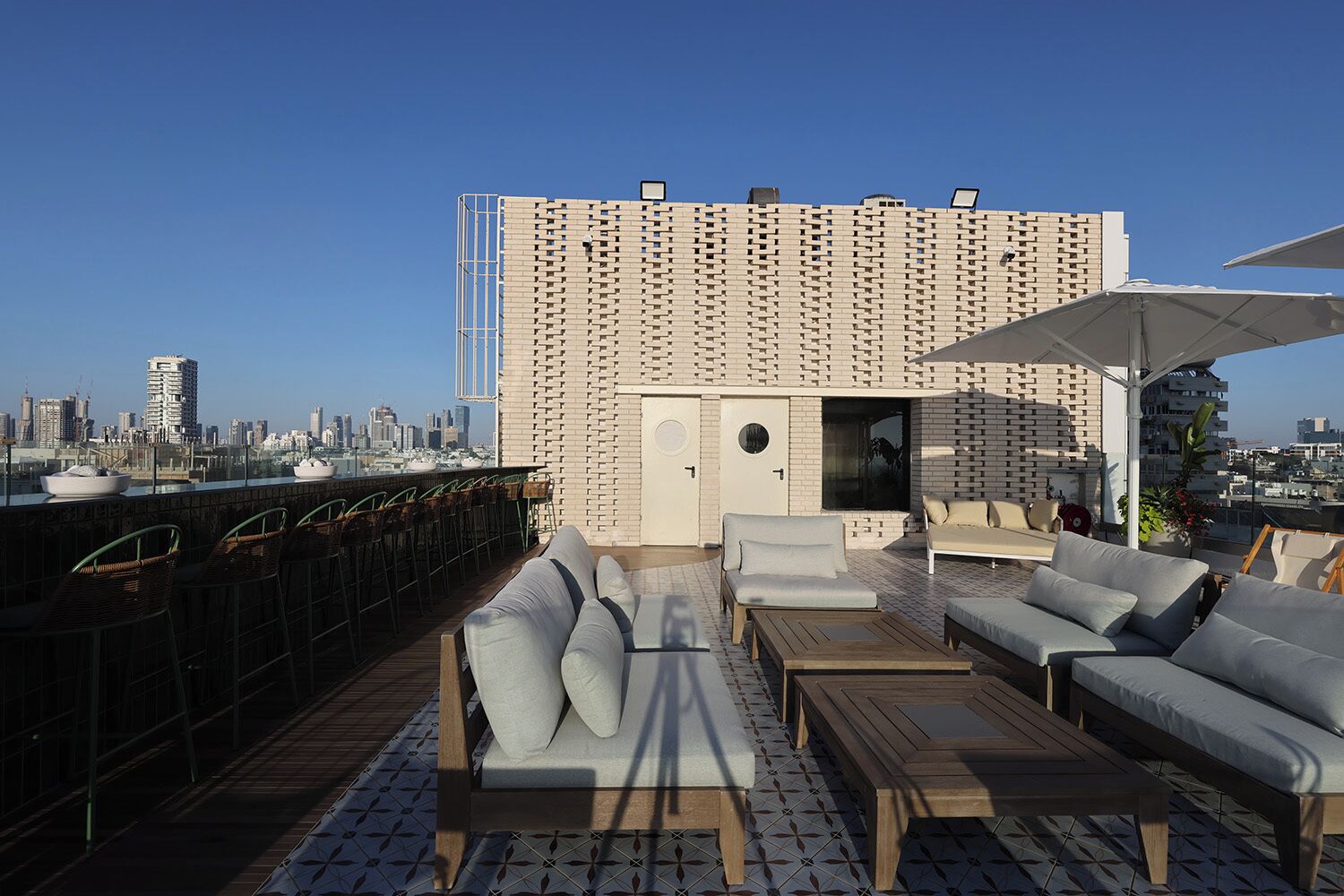 Une terrasse sur le toit offrant une vue panoramique sur la ville, avec un mur décoré de motifs, des sièges d’extérieur et un espace bar.