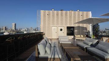 A rooftop terrace with a city skyline view, featuring a patterned wall, outdoor seating, and a bar area.