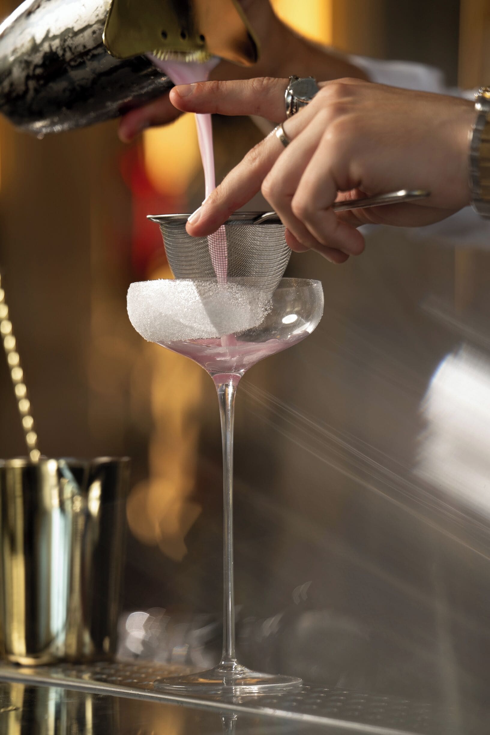 A person pouring a drink into a martini glass with a sugar rim.