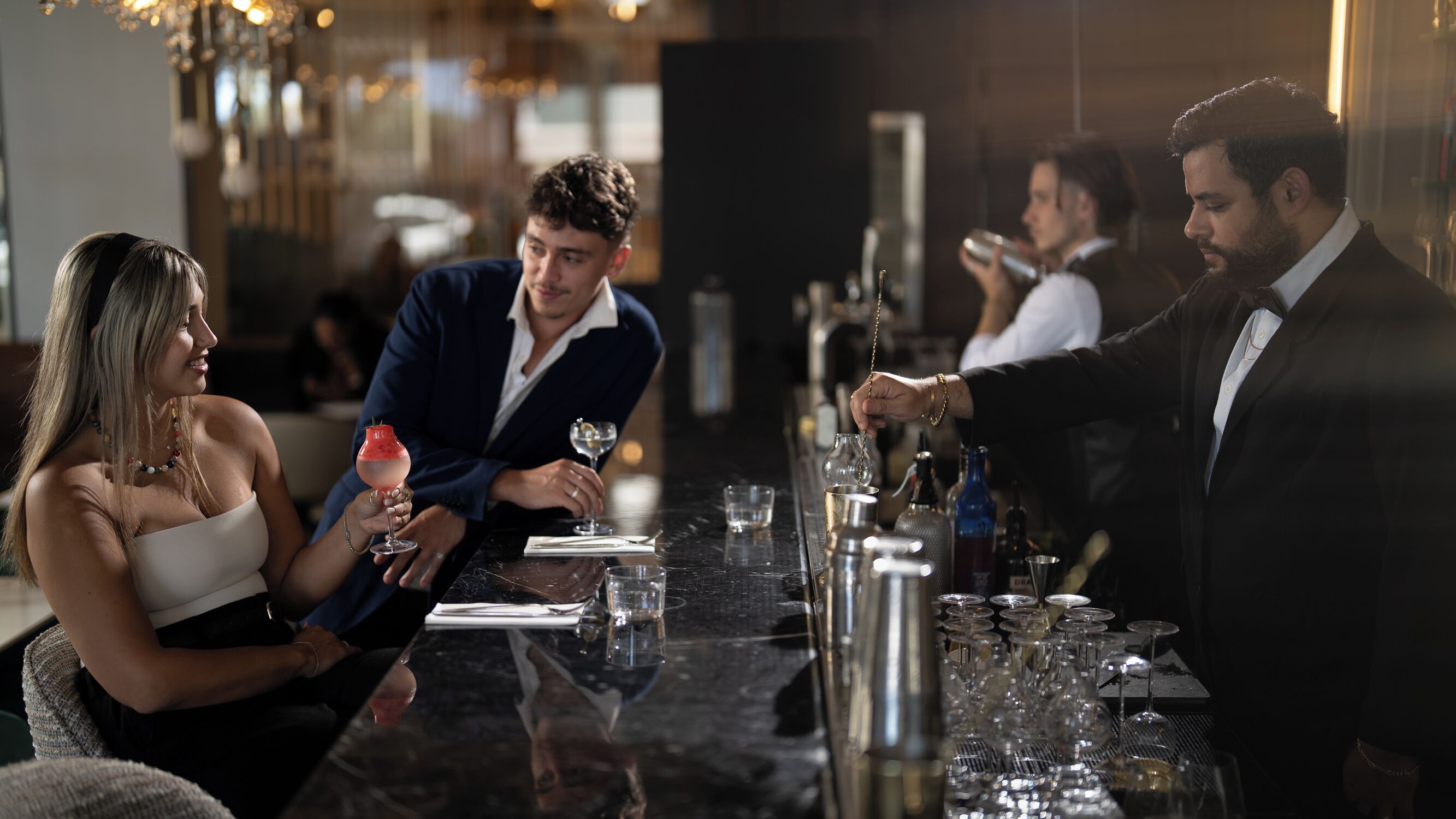 Un bar con mostrador de mármol, vasos y botellas.