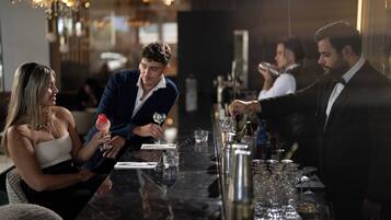 Un bar con mostrador de mármol, vasos y botellas.