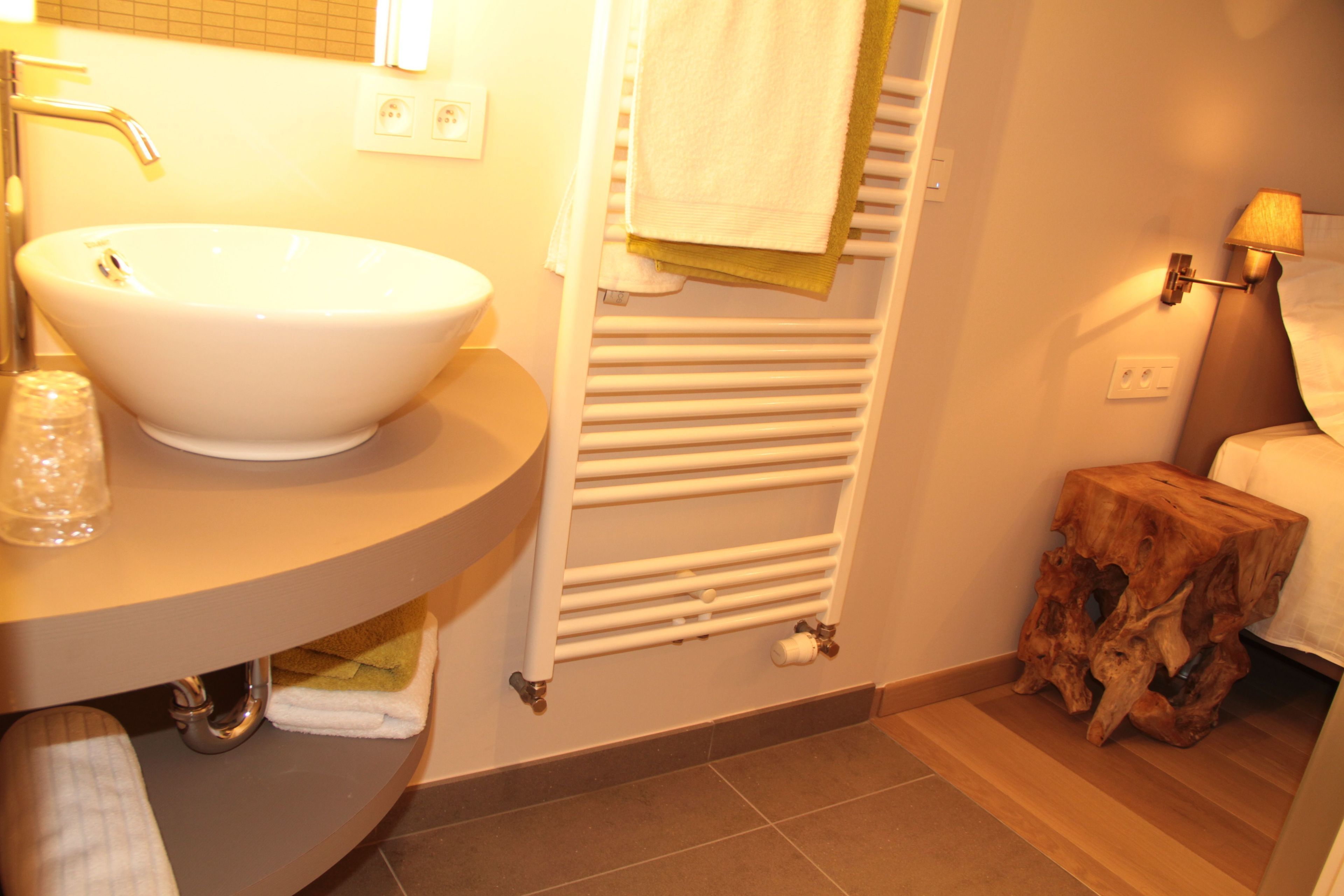 A bathroom with a white sink, a towel rack, a wooden stool, and a wall-mounted lamp.