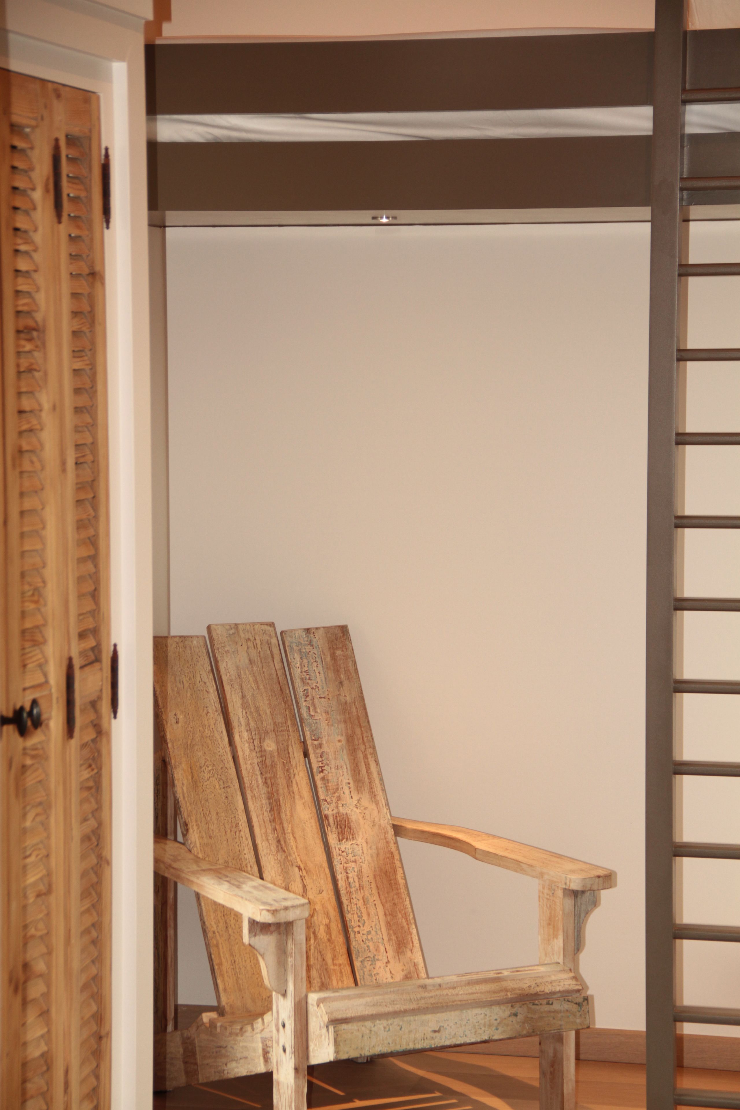 Une chaise en bois appuyée contre un mur, dans une pièce qui contient une porte et une échelle en métal.