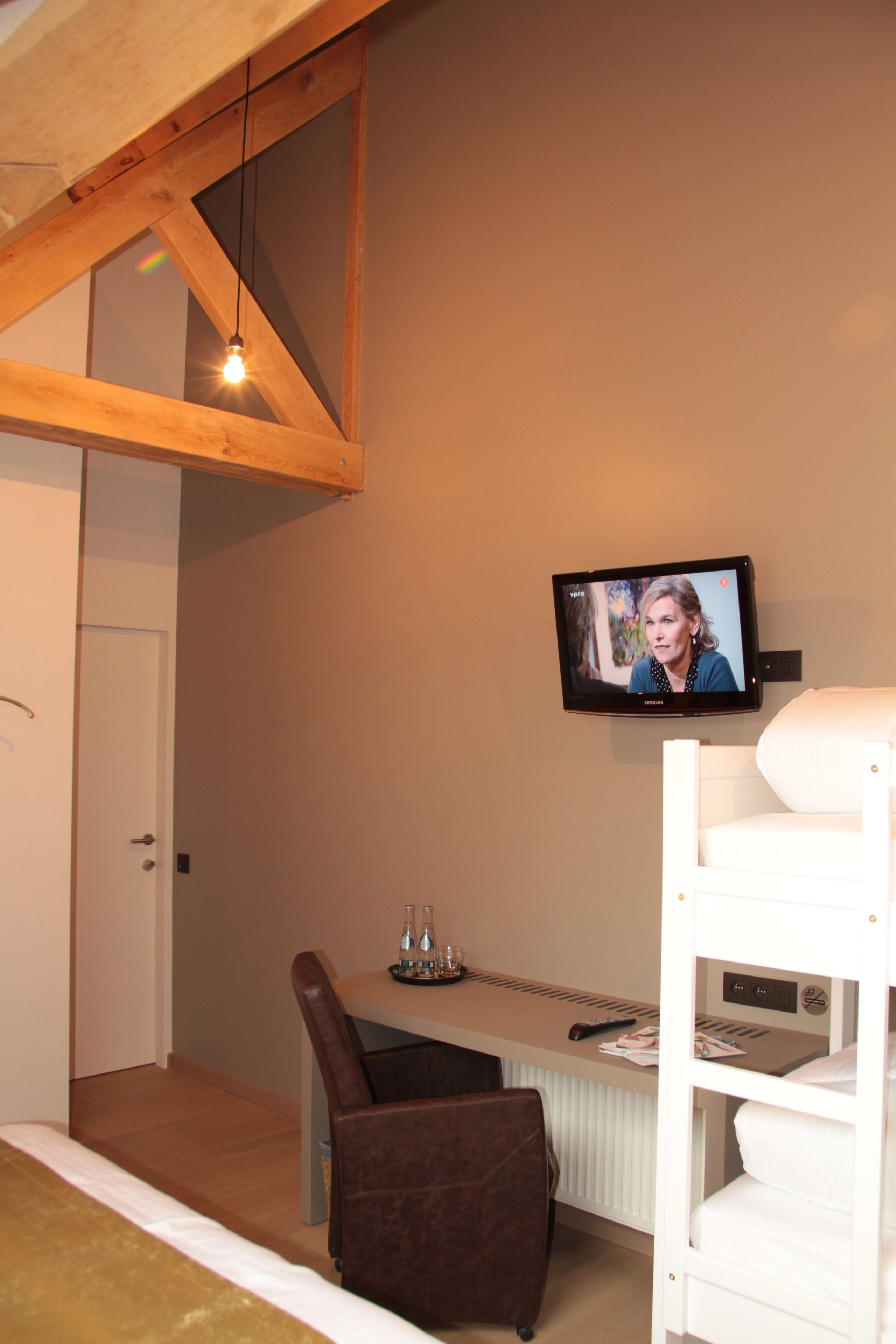 A room with a bunk bed, a desk with a computer, a chair, and a television mounted on the wall.