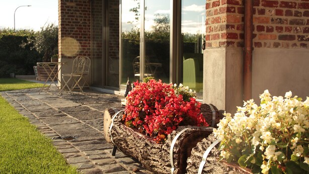Un bâtiment en briques doté d’un patio, d’un banc en bois agrémenté de fleurs et d’une chaise.