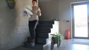 Une personne descend un escalier dans un bâtiment. On aperçoit un extincteur et un pot de fleurs près de l’entrée.