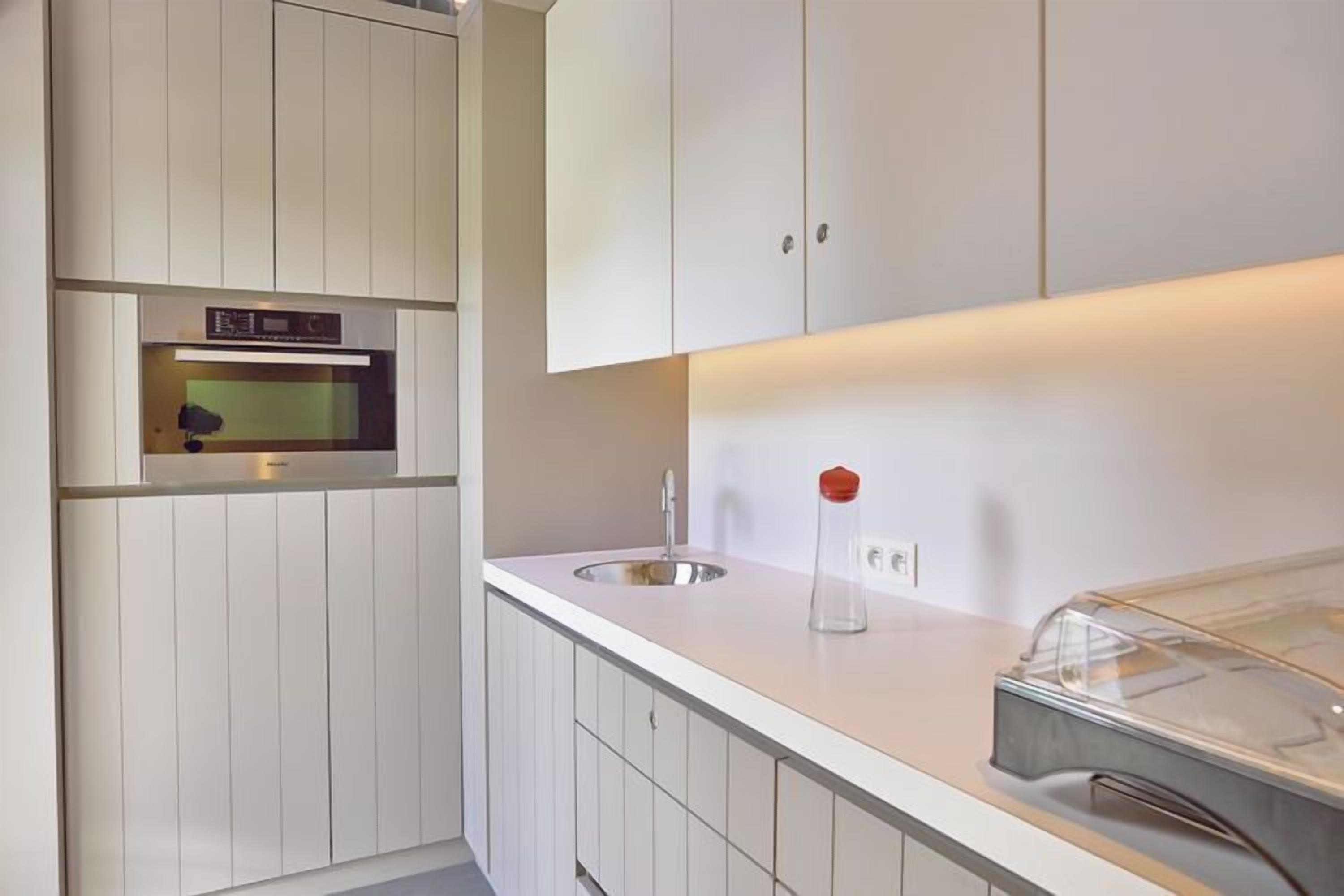 Een moderne keuken met witte kastjes, een inbouwoven, een spoelbak en een glazen pot op het aanrecht.