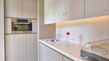Een moderne keuken met witte kastjes, een inbouwoven, een spoelbak en een glazen pot op het aanrecht.