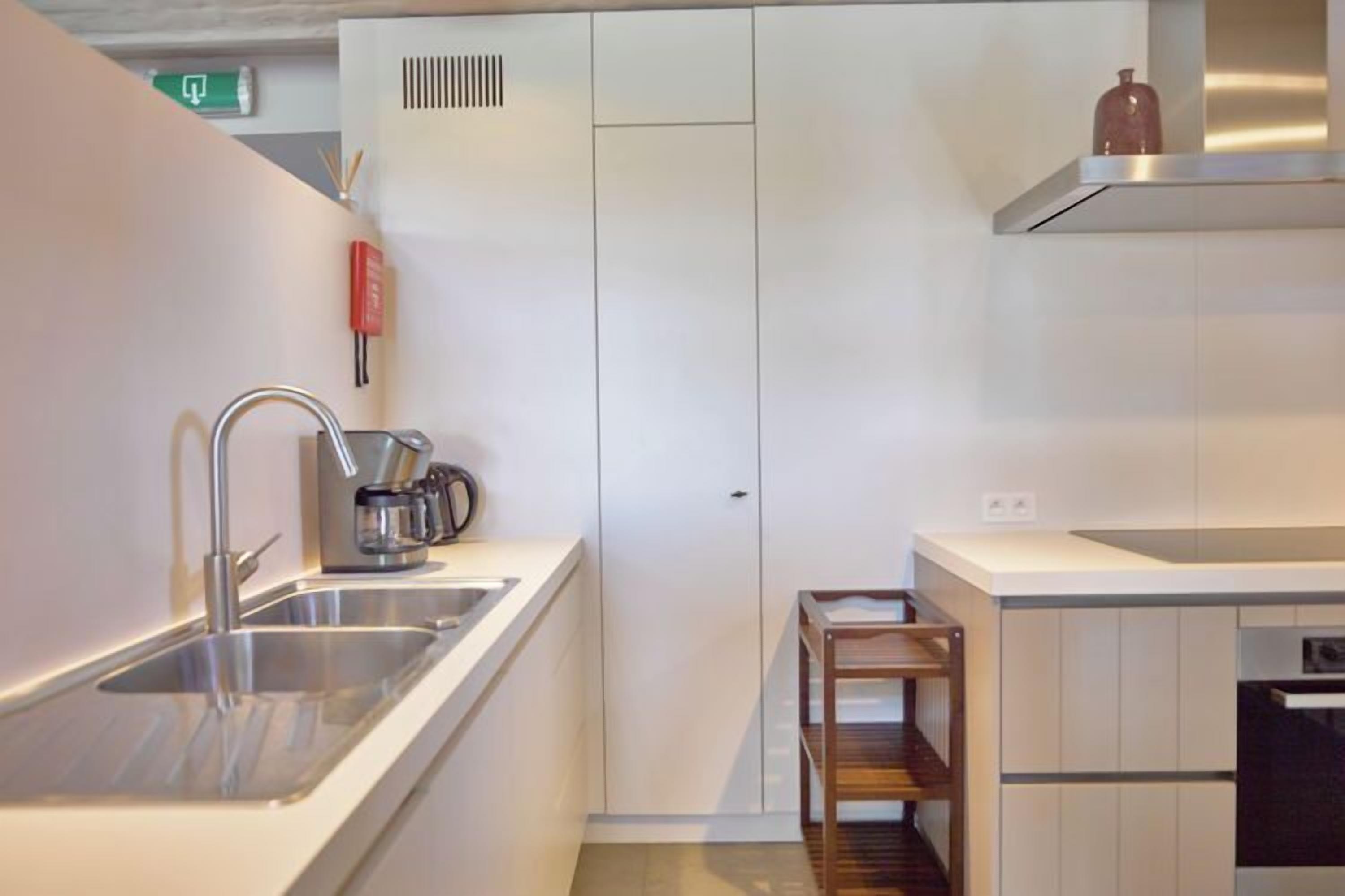 A modern kitchen with stainless steel appliances, a built-in oven, and a wooden shelf.