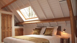 Une chambre avec un puits de lumière, des poutres en bois, un lit avec des oreillers, une table de chevet et une petite table de nuit avec une lampe.