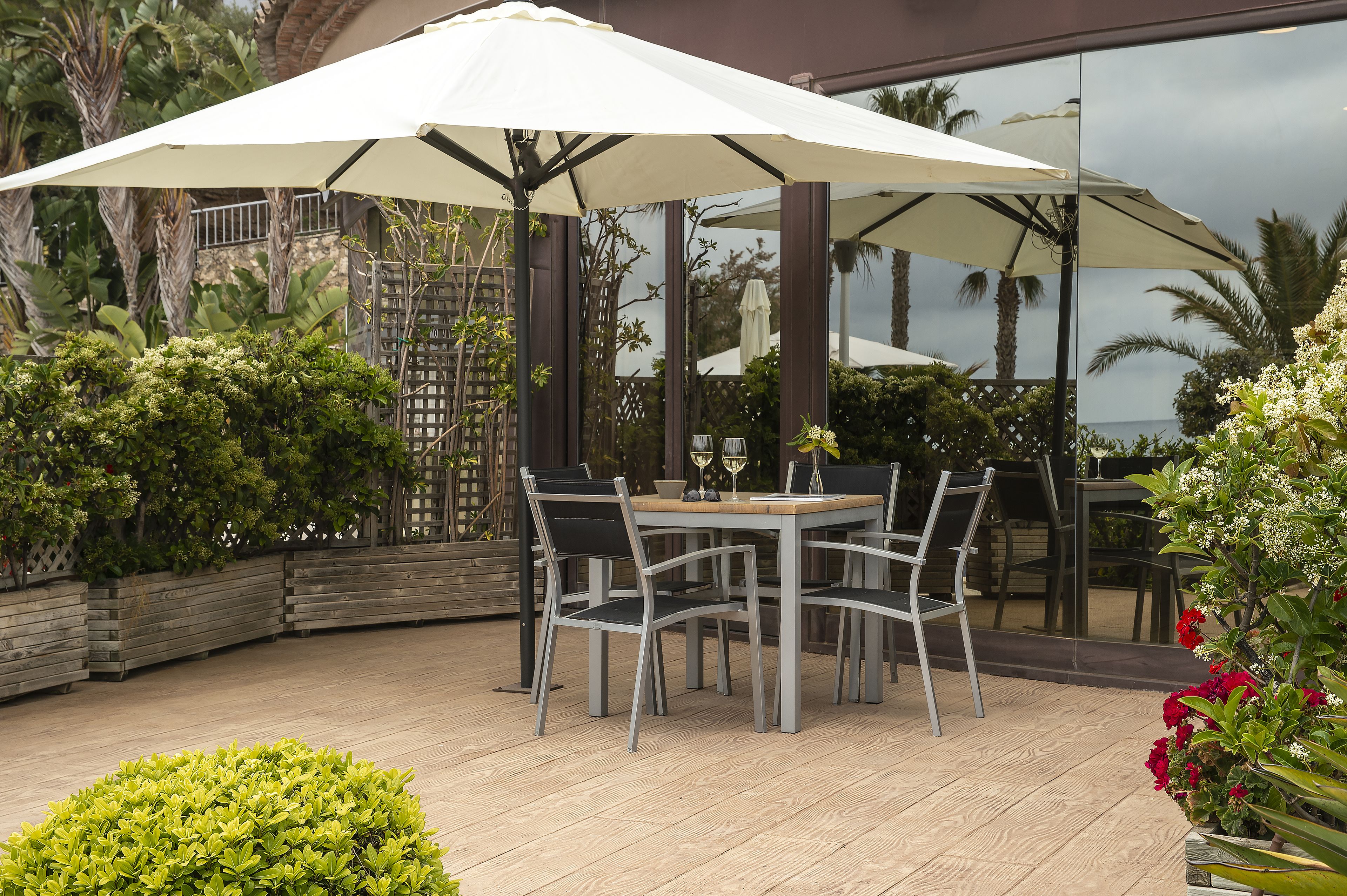 An outdoor patio with a table and chairs, surrounded by plants and umbrellas.