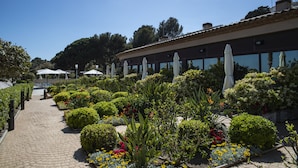 A garden pathway leading to a building with outdoor seating and umbrellas. - Cala Cristal by Pierre & Vacances Premium (Mont-roig del Camp)