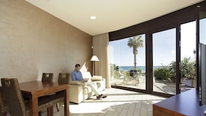 A modern hotel room with a dining area, a sofa, and a large sliding glass door leading to a balcony with a view of the sea. - Cala Cristal by Pierre & Vacances Premium (Mont-roig del Camp)