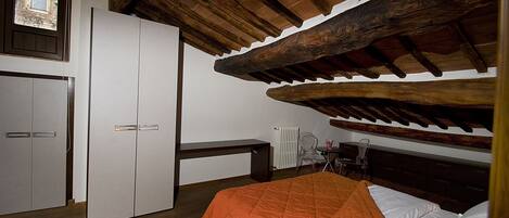 Una camera da letto con soffitto in legno, un letto con coperta arancione, un armadio bianco e una scrivania con sedia.