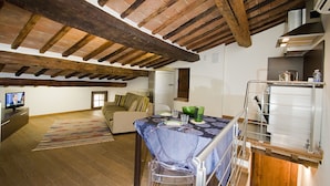 Un loft spacieux avec des poutres apparentes, un coin repas avec une table dressée pour deux personnes, un canapé et un téléviseur dans l’espace de vie.