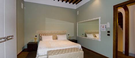 Un dormitorio con cama, banca, mesita de noche, espejo y puerta.