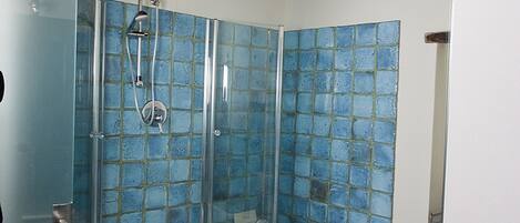 Une salle de bain avec une douche à parois de verre, une baignoire blanche et un lavabo également entouré de parois de verre.