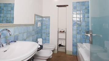 A bathroom with a white sink, two toilets, a bathtub, and blue-tiled walls.