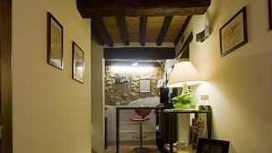 Un couloir étroit au sol en pierre, avec des poutres en bois au plafond et des tableaux encadrés accrochés aux murs.